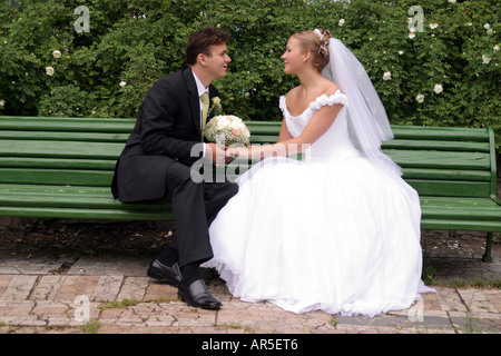 Un couple nouvellement marié tenant les mains sur un banc de parc. Banque D'Images