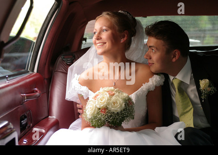 Un couple nouvellement marié dans leur voiture de mariage. Ils sont à la fois souriant et heureux à la recherche. Banque D'Images