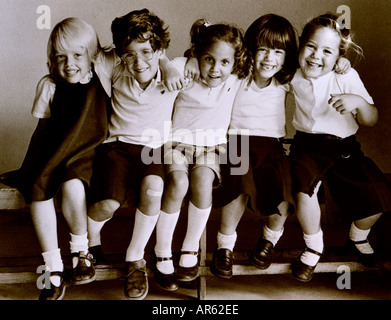 Groupe scolaire junior 1980 rétro vintage de heureux 7-11 ans enfants de l'école junior en uniforme assis sur le banc de la classe rétro de l'école de jour B & W Banque D'Images