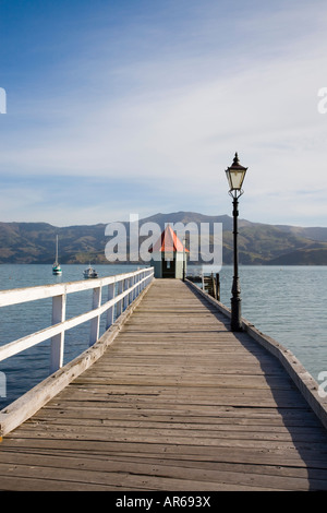 Vue le long du quai avec petit Daly toit rouge à la fin de la construction de la jetée en bois et vue sur la baie d'Akaroa Harbour en Nouvelle Zélande Banque D'Images