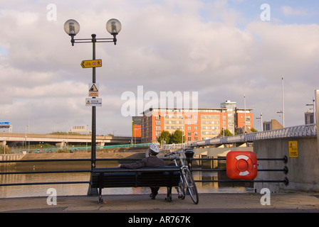 Lagan Weir homme est assis sur un banc au bord de la rivière Lagan n Belfast irlande du nord système de contrôle du niveau de l'eau fond de ciel bleu b s Banque D'Images