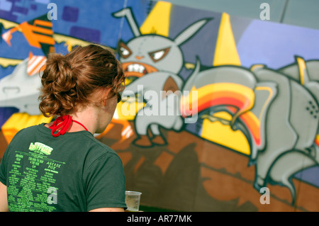 La jeunesse d'un jeune homme de pulvériser un mur de graffiti en orange et d'autres couleurs Banque D'Images