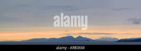 Coucher de Mull, avec le continent et l'île d'Eigg, Muck et le rhum dans la distance. Un phare est visble sur le continent Banque D'Images