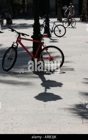 Deux vélos en stationnement et un étant montés dans une place de la ville en Espagne. La composition est rétro-éclairé et bien apparaît en silhouette Banque D'Images