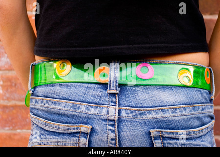 Petite fille en Jean avec ceinture élégante et colorée. Mains dans les poches. Banque D'Images