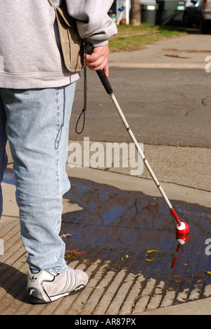 Femme Aveugle trouve une flaque d'eau avec sa canne blanche à un bateau de trottoir Banque D'Images