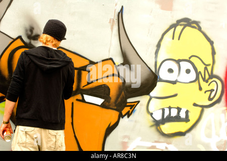 La jeunesse d'un jeune homme de pulvériser un mur de graffiti en orange et d'autres couleurs Banque D'Images