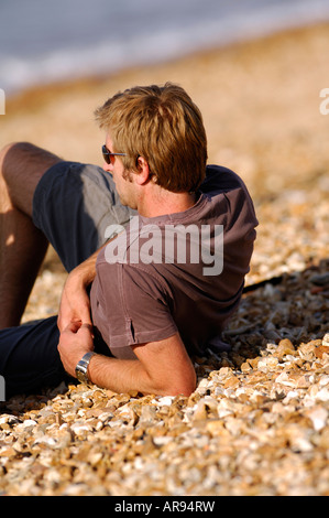 Un homme étendu portant sur la plage dans le soleil d'été sur le port de lunettes de soleil les cailloux relaxing Banque D'Images