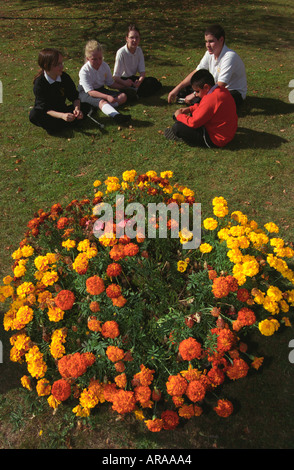 Groupe de personnes ayant des enfants de l'école détente sur pelouse au terrain de l'école, en Angleterre. Banque D'Images