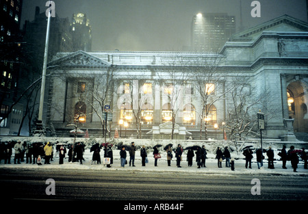 Une file d'attente à un arrêt d'autobus dans la neige à l'extérieur de la Bibliothèque publique de New York à New York USA Banque D'Images