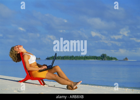 Femme assise sur la chaise de plage avec tête en arrière et fermé les yeux sur le travail avec ordinateur portable en vacances Maldives Banque D'Images