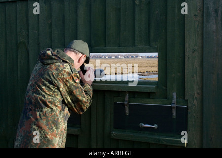 Observateur d'oiseaux côtiers, habillé en vert, à l'aide de la portée de cacher à Sandside, Marshside la réserve RSPB, Southport, Merseyside, Royaume-Uni Banque D'Images