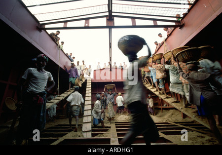 Décharger les travailleurs un navire rempli de sable en transportant le sable dans les paniers en osier sur la tête qui sera utilisé pour faire le ciment Banque D'Images