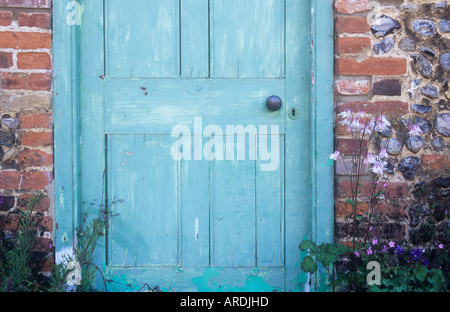 Détail de la porte en bois lambrissé vert pâle avec poignée en laiton et avec des murs en briques et silex de chaque côté avec des fleurs Banque D'Images