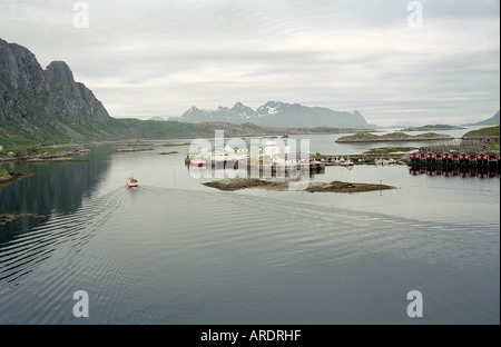 Un petit bateau de pêche de quitter le port de Svolvær passé une rangée de cabines en bois rouge traditionnel Banque D'Images