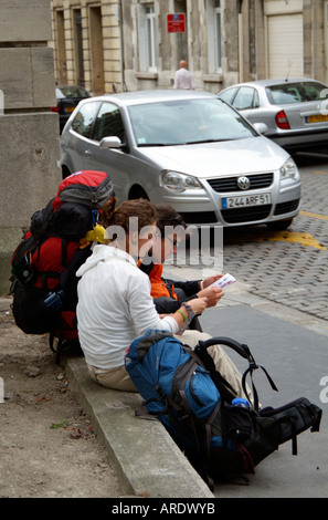 Les jeunes backpackers assis sur le bord de la route de la lecture d'un livre guide touristique. Banque D'Images