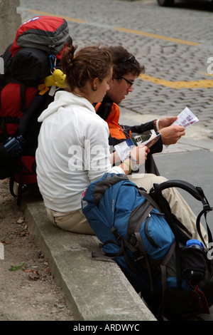 Les jeunes backpackers assis sur le bord de la route de la lecture d'un livre guide touristique. Banque D'Images