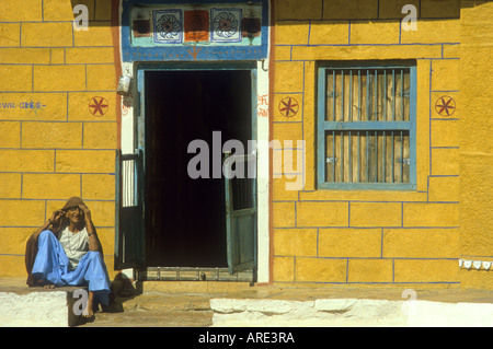 Femme de la localité se trouve dans le soleil à l'extérieur de sa chambre aux couleurs lumineuses près du grand désert du Thar au Rajasthan, Inde Banque D'Images