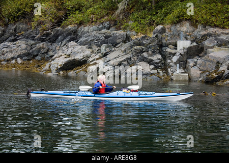Femme kayak le long de la rive en Johnstone Sound près de Telegraph Cove, l'île de Vancouver, Canada Banque D'Images