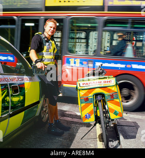 Paramedic de la London Ambulance Service debout en voiture et vélo comme un laissez-passer d'autobus rouge à Londres en Angleterre Banque D'Images