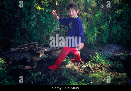 Jeune garçon portant des bottes wellington palying muddy stream Banque D'Images