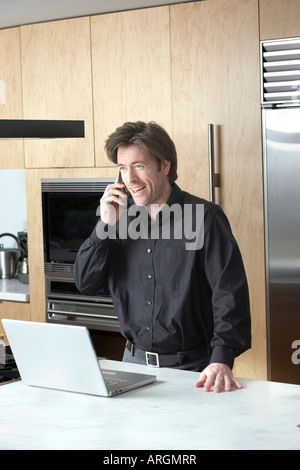 Homme avec portable et téléphone cellulaire dans la cuisine Banque D'Images