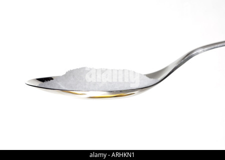Sucre sur une cuillère à café en acier inoxydable sur un fond blanc. Banque D'Images