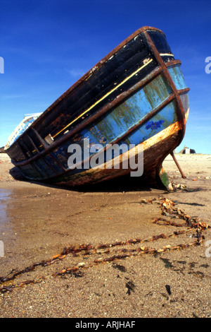 Un bateau de pêche abandonnés repose sur la plage à l'île de Lindisfarne UK, avec les chaînes rouillées au premier plan. Banque D'Images
