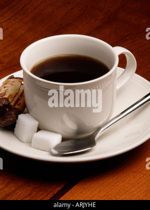 Tasse de café en porcelaine blanche sur table en bois avec des morceaux de biscuits de sucre et cuillère Banque D'Images