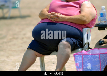 Très grosse femme assise sur une chaise sur une plage Banque D'Images