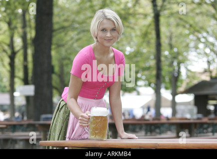 Jeune femme blonde portant une robe dirndl Tegernsee tradional mettre une chope de bière sur la table dans un biergarten de Munich Banque D'Images