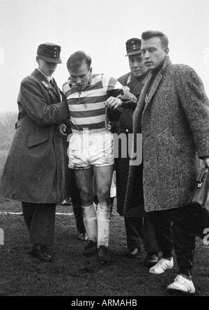 Football, DFB, huitième final, 1964/1965, stade de Duisburg Wedau, Meidericher SV contre l'Eintracht Brunswick 0:1 blessés, joueur de football, Werner Kraemer (Duisburg) est dirigé à partir de la hauteur par deux ambulancemen et un masseur de Duisburg (droite) Banque D'Images