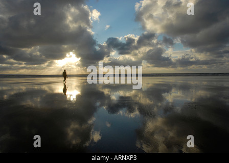 Une silhouette solitaire walker dans le sable humide sur Saunton Beach North Devon, Angleterre Banque D'Images