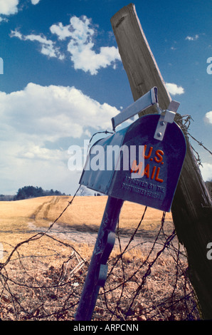 Old US mail box appuyé contre un poste en bois le long d'un pays désert chemin de terre et un champ de l'été l'herbe sèche et ciel bleu Banque D'Images