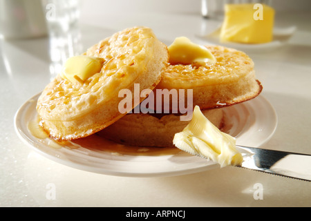 Hot buttered toast traditionnel des crumpets sur une plaque blanche sur une table, avec du beurre fondu prêt à manger Banque D'Images
