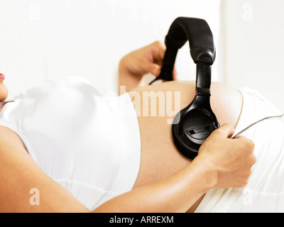 Femme enceinte avec un casque plus de ventre sur canapé Banque D'Images