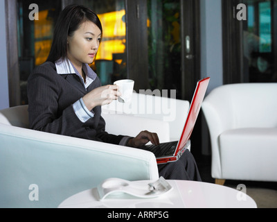 Businesswoman holding cup while using laptop Banque D'Images