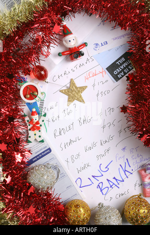 Factures, relevé bancaire, guirlandes, décorations de l'arbre et de carte de crédit entourent une liste de Noël. Banque D'Images