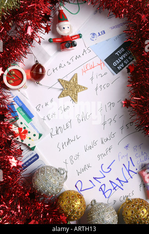 Factures, relevé bancaire, guirlandes, décorations de l'arbre et de carte de crédit entourent une liste de cadeau de Noël. Banque D'Images