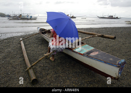 Une femme attend pour les pêcheurs d'accoster au petit matin sur une plage à Mansalay, Oriental Mindoro, Philippines. Banque D'Images