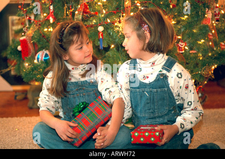 Soeurs en salopette age 8 et 6 holding wrapped Christmas gifts par un arbre décoré. St Paul Minnesota USA Banque D'Images