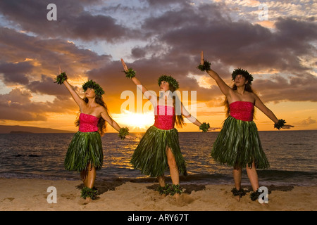 Trois danseurs hula dans ti leaf jupes danse sur la plage au coucher du soleil à Makena, Maui. Banque D'Images