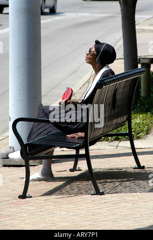 Une vieille femme noire est assise sur un banc de la rue portant des écouteurs et écouter son lecteur CD Banque D'Images