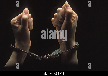 Les mains de la femme emprisonnée dans les tenailles d'poings menottés et silhouetté sur fond noir Banque D'Images