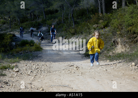 Fille courir en avant de sa famille sur un chemin de terre pendant qu'ils derrière cycle, Vitrolles, Aix en Provence, France. Banque D'Images