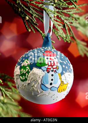 Boule bonhomme de neige traditionnelle de Noël décorée de façon festive pendant un Noël arbre avec lumières derrière Banque D'Images