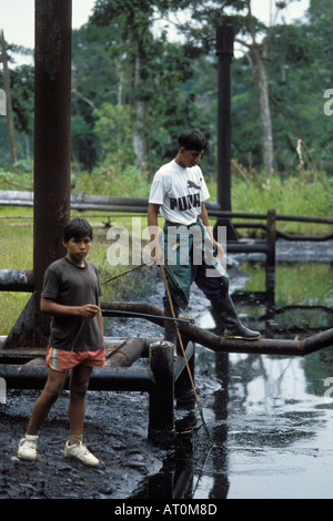 Deux jeunes garçons Warane regardent les déchets pétroliers éliminés par l'industrie pétrolière Équateur Amérique du Sud Amazon Banque D'Images