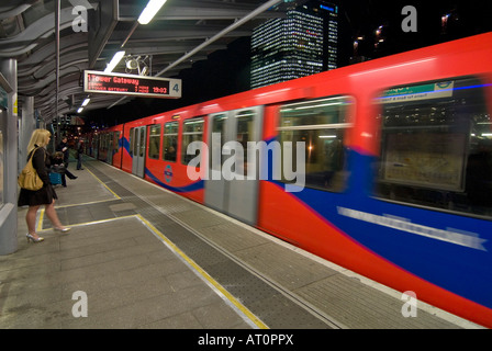 Grand angle horizontal d'un Docklands Light Railway train arrivant en gare de peuplier avec des gens qui attendent sur la plate-forme dans la nuit Banque D'Images