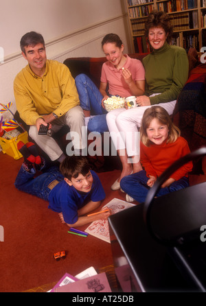 Famille des années 1990 regardant la télévision, style de mode rétro de l'ère des années 90, deux filles 11ans et 6ans garçon 5 ans, regarder la télévision ensemble joyeusement relaxant à leur maison au Royaume-Uni Banque D'Images