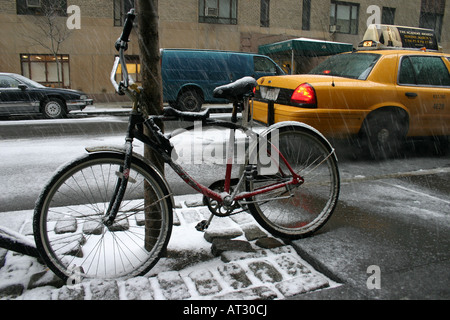 Un vélo dans la neige comme un taxi attend dans la rue, l'upper west side de Manhattan, New York City, USA Banque D'Images